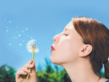Pretty woman blowing dandelion on the meadow