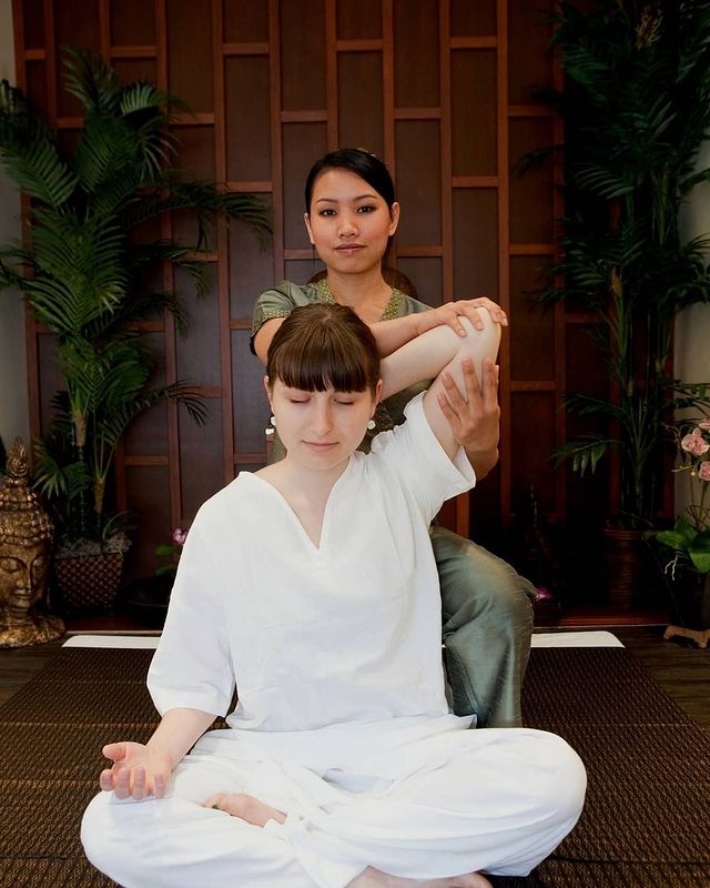 Asian massage specialist lifting the left arm of a woman